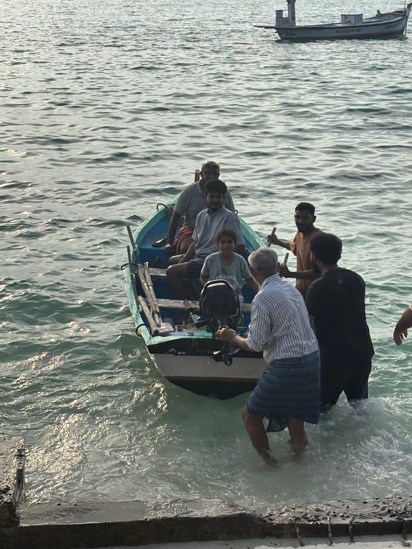 Islanders helping passengers off a small wooden boat at a Lakshadweep jetty