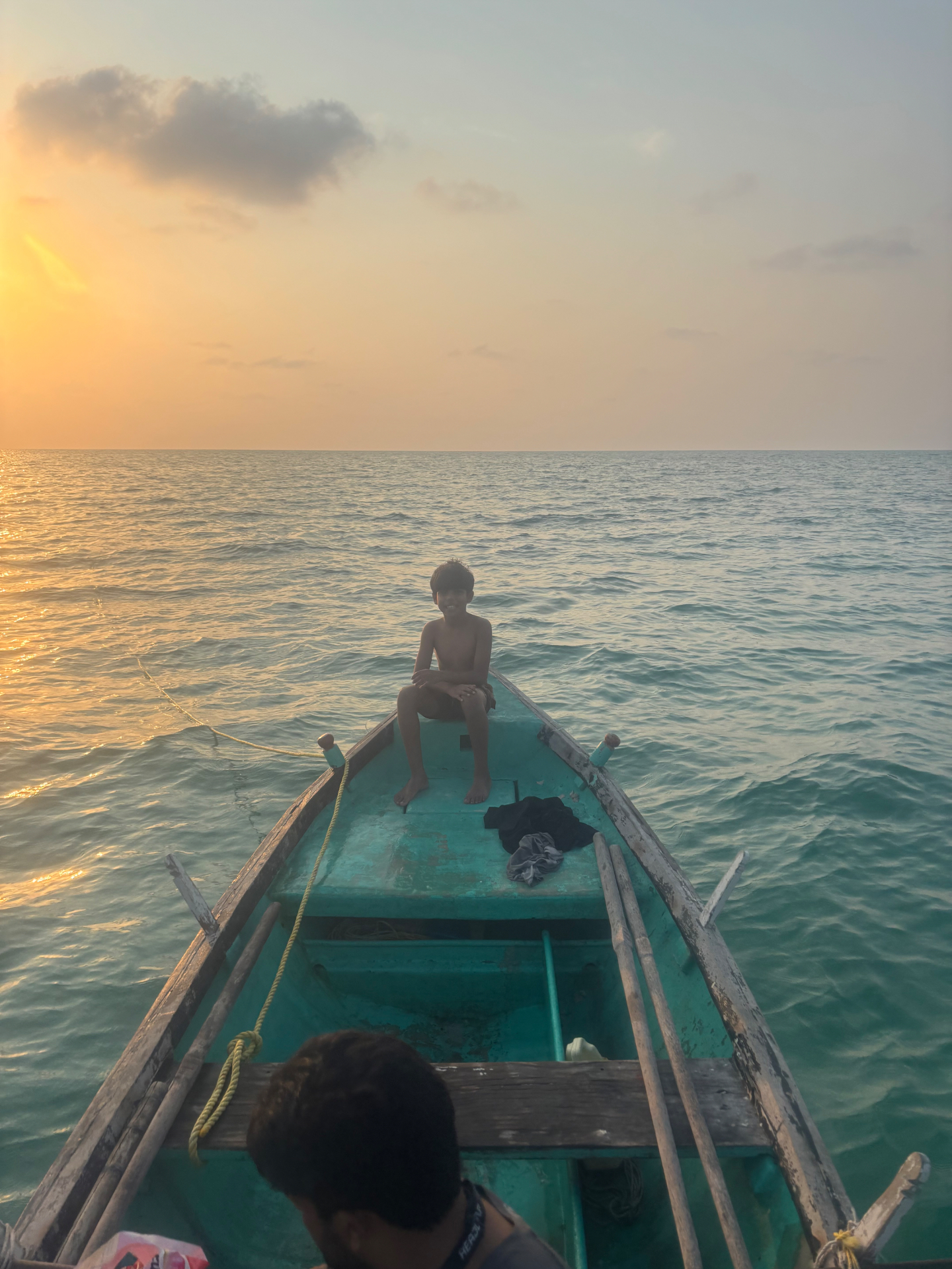A child on the bow of a wooden boat at sunset off the Lakshadweep coast